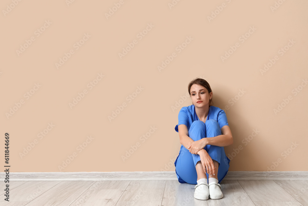 Sad female medical intern sitting near beige wall