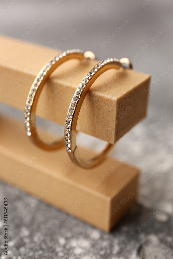 Decorative podium with beautiful golden earrings on grunge grey background