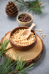 Pine nuts in a bowl on a wooden board on a blue texture background with branches of pine needles and a cone close up. The concept of a natural, organic and healthy superfood