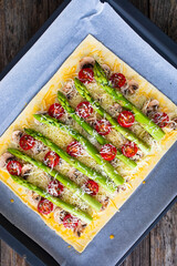 Poster - Uncooked puff pastry, green asparagus with mozzarella cheese, mushrooms and cherry tomatoes on baking paper on cooking pan
