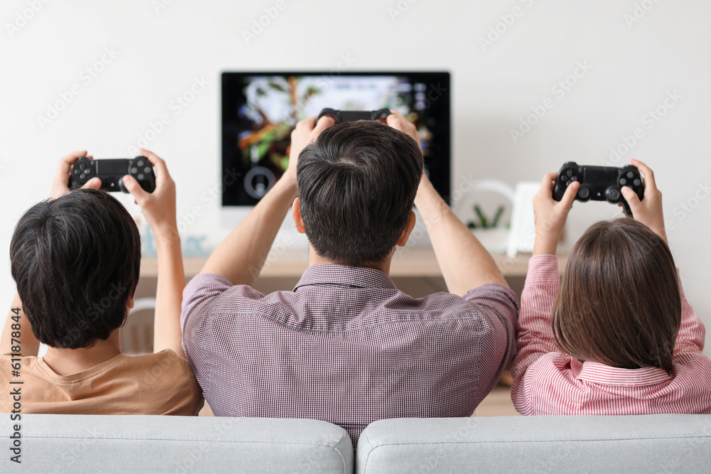 Father with his little children playing video game at home, back view