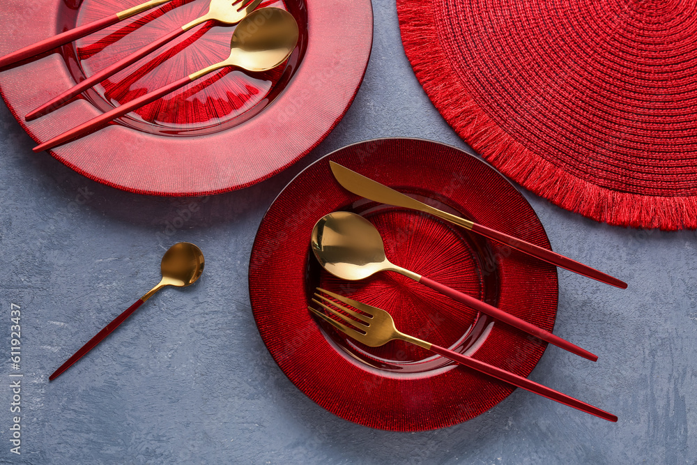 Golden cutlery with red plates and kitchen mat on blue grunge background