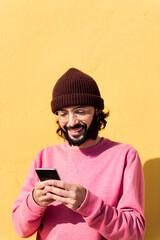 smiling young man using mobile phone in a yellow background, concept of technology of communication 