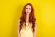 Offended dissatisfied  young redhead woman wearing  yellow t-shirt over yellow wall with moody displeased expression at camera being disappointed by something