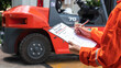 A mechanical engineer is using heavy equipment checklist form for inspecting the factory forklift vehicle (as blurred background). Industrial working with safety practice concept, selective focus. 