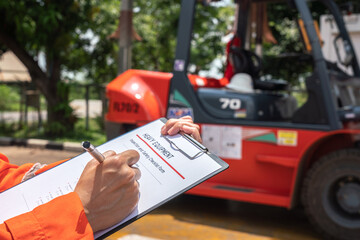 A mechanical engineer is using heavy equipment checklist form for inspecting the factory forklift vehicle (as blurred background). Industrial working with safety practice concept, selective focus. 