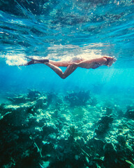 A woman snorkeling over coral in blue waters