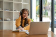 © Natee Meepian - Young woman having video call on her computer at home. Smiling girl studying online with teacher