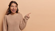 © wayhome.studio  - Latin woman commands attention with confident gesture pointing towards open copy space inviting viewers to embark on journey of discovery wears knitted jumper isolated over brown background.