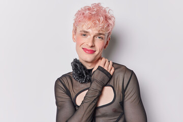 Pink haired stylish gay man wears makeup captures essence of his unique identity with every pose smiles gently has tender expression wears black jumper with holes isolated over white background