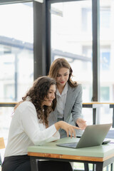 Wall Mural - Businesswoman and accountant talking with laptop and tablet Two attractive millennial caucasian businesswoman planning project together at table in office