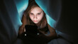 © golubovy - Child addiction. Online night. Focused serious obsessed girl lying hiding with smartphone under blanket watching content at bedtime at home.