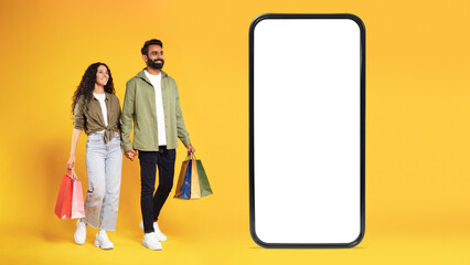 Wall Mural - Arabic Couple With Shopping Bags Posing Near Smartphone, Yellow Background