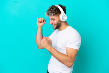 Wall Mural - Young handsome caucasian man isolated on blue background listening music and dancing