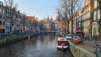 Wall Mural - Amsterdam, Netherlands - April 22, 2023: Discovering the city of Amsterdam in spring days. Biking around Amstel river, old houses and nice view to the old part of the city.