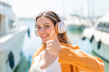 Wall Mural - Young pretty woman at outdoors listening music and with thumb up