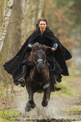 Wall Mural - Beautiful woman in historical costume riding fast on horseback over puddles