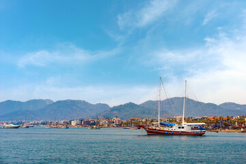 Sailboat in the sea over mountains and seaside resort town background. Summer vacation, adventure, travel, active leisure.