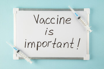 Wall Mural - overhead view of vaccine is important writing on white desk and disposable syringes on blue backgrou