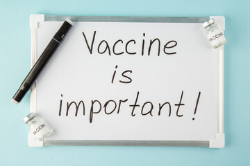 Wall Mural - top view of vaccine is important writing on white desk and pen medicine on blue background