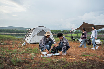 a group of tourists camping by the river and the forest, collecting trash around the camp site, to r