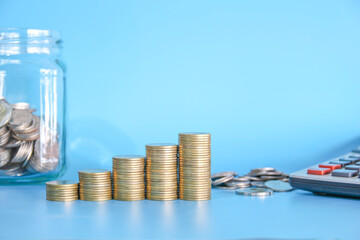 Stack of golden money con on blue background with coin in the glass jar and calculator. Saving money or finance concept. 