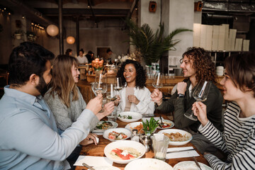 Wall Mural - Group of joyful friends talking and drinking wine while dining in restaurant