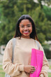 © Jose Calsina - Vertical individual portrait of a happy hispanic smart school girl with glasses smiling and laughing out of class holding the notebook. Cute teenage student standing at the university campus. High