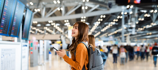 young asian woman in international airport, using mobile smartphone and checking flight at the fligh