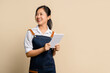 © PBXStudio - Start a small business, Young smiling asian businesswoman in apron with laptop holding laptop standing isolated on light brown background.