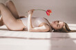 young attractive redhead woman lie in bed closed breast by tulip. Minimalist light pure shoot. Concept of female health, menstrual cycle and ovulation. Allegorical depiction of defloration. Top view