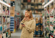 © Westend61 - Young woman using phone while shopping at supermarket