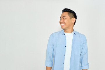 Smiling young Asian man in casual clothes looking aside at copy space with happy expression isolated on white background