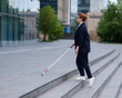 © Михаил Решетников - Blind business woman in glasses and with a cane climbs the stairs to the business center.