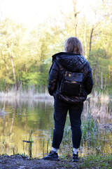 girl walking in the woods, stands by the lake, back view. young woman in spring forest. girl with a backpack, tourist. enjoying spring weather. Rest, lifestyle, walk in the fresh air. hiking in nature