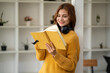 © Wuttichaik - Young Beautiful smiling happy student woman wearing headphone holding a book, Portrait of student girl carry book balancing books on head and hand