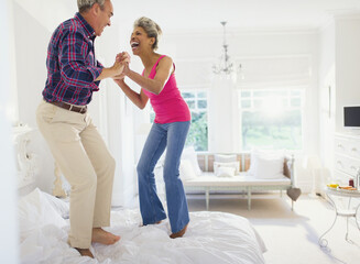 Canvas Print - Playful mature couple jumping on top of bed