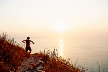 Canvas Print - Male runner backpack descending craggy trail overlooking sunset ocean