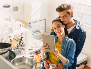 Wall Mural - Affectionate young couple using digital tablet in apartment kitchen