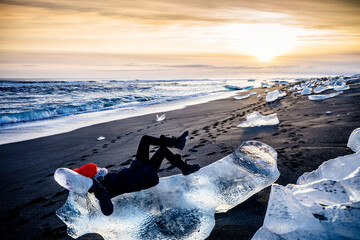 Wall Mural - Woman laying on large ice chunk on beach at sunset, Iceland