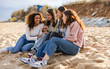 © PintoArt - Young multiracial women laughing out loud on a sunny day - Cheerful group female friends enjoying summer vacation together on the beach sitting down- Summer vacation