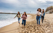© PintoArt - Portrait of excited young female friends running on the beach. Multiracial group of friends enjoying a day at the beach.