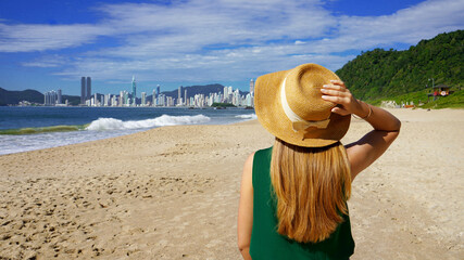 Wall Mural - Holidays in Brazil. Panoramic view of traveler girl on Praia do Buraco beach with Balneario Camboriu skyline, Brazil.