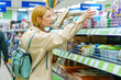 © Pokoman - A beautiful girl chooses a product in the store. The girl examines the products on the shelf of the shopping center. window shopping