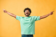 Victory celebration. An emotional handsome young man with curly hair in a turquoise T-shirt on a yellow background points his hands to the side and shouts. The emotion of happiness, joy, laughter.