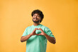 © HBS - An image of an Indian man in a turquoise t-shirt showing a gesture of heart, love, affection, care with his fingers and smiling while looking at the camera.