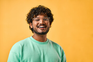 close-up portrait of a handsome curly-haired indian man in a turquoise t-shirt and glasses laughing 