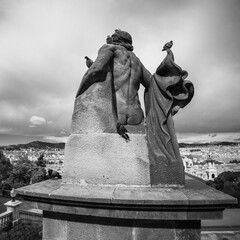 Sticker - Grayscale of sculpture of a naked man in height, cityscape under the gloomy clouds