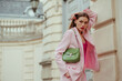 Fashionable elegant confident woman wearing trendy pink suit blazer, trousers, with green faux leather shoulder bag, posing in street. Outdoor fashion portrait. Copy, empty space for text