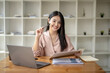 © Wasana - Happy smiling business woman working with laptop computer with paperwork at desk in a modern office, business finance technology concept.
